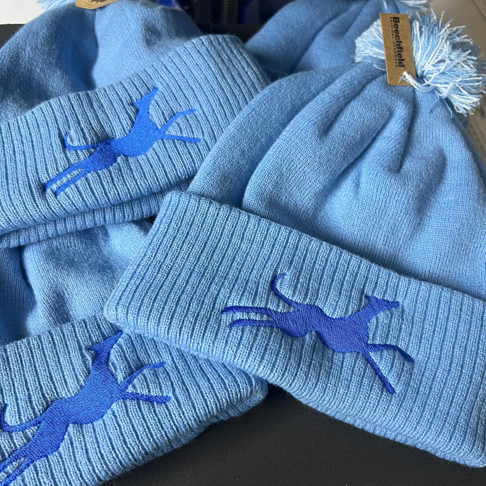 Blue bobble hats with embroidered designs on a dark surface. Made at The Wrong End of Town in Dover, Kent.