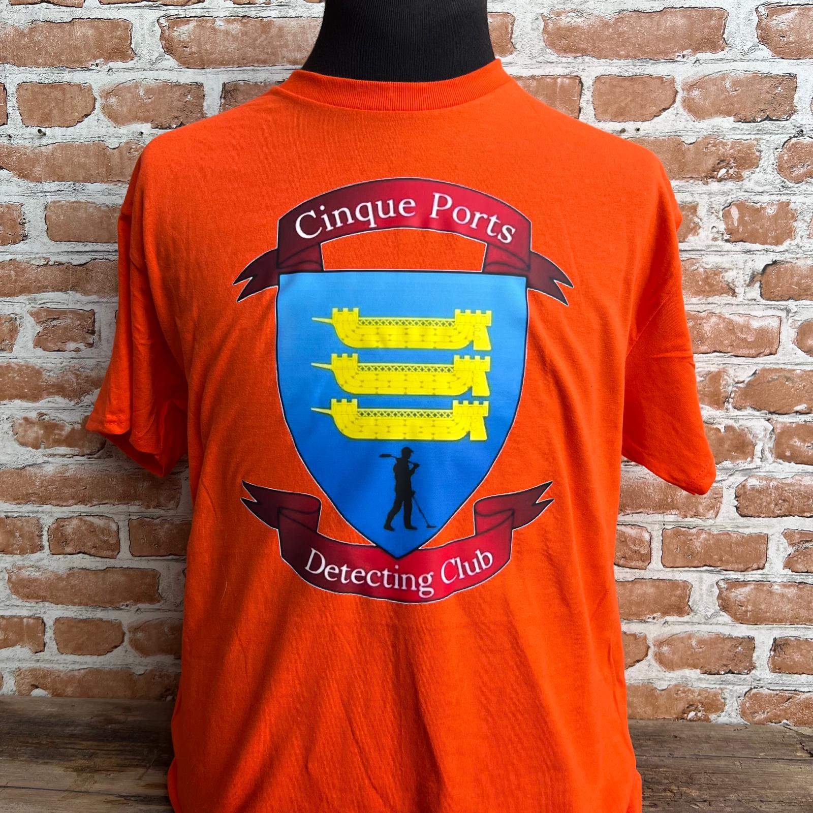 Orange t-shirt with a crest and text displayed against a brick wall. Made by The Wrong End of Town in Dover, Kent.