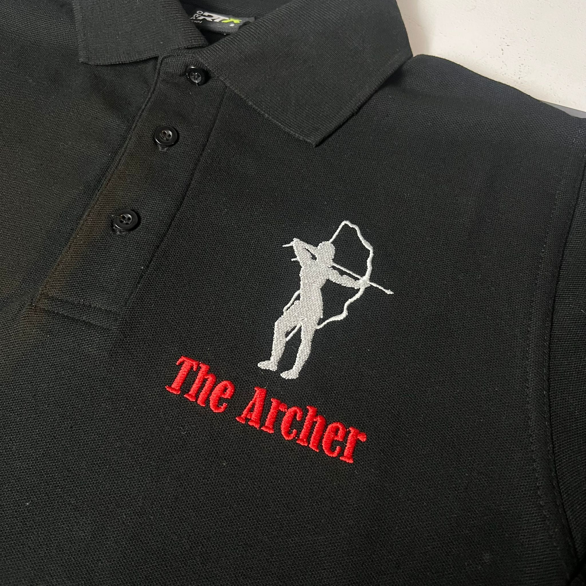 Black polo shirt with 'The Archer' logo on a white background. Made by The Wrong End of Town in Dover, Kent.